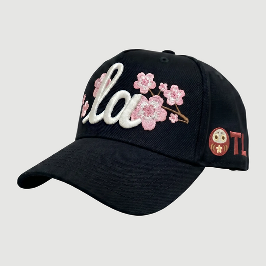 Black cap with cherry blossom design and brand logo on a light gray background